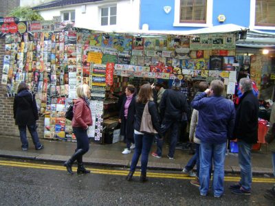 Turistas observando uma barraca cheia de placas e pôsteres no Portobello Road Market em Notting Hill, Londres
