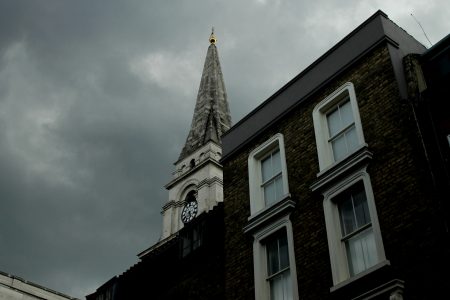 Torre de igreja histórica em Londres com relógio e céu nublado ao fundo.