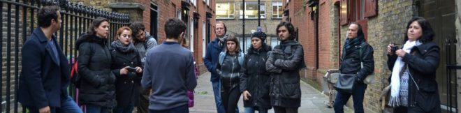 Grupo de turistas em passeio guiado por ruas históricas de Londres, ouvindo explicações do guia.