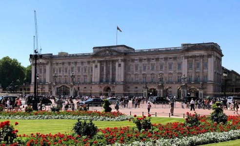 palacio de buckingham com muit agente na frente e bandeira estandarte real com a rainha elizabeth ii em residência e jardins floridos em londres