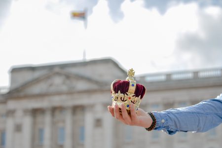 mão segurando coroa pequena na frente do palácio de buckingham com a rainha em londres
