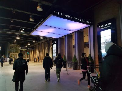 Entrada iluminada da The Shard Viewing Gallery em Londres com visitantes passando.