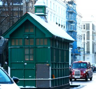 casinha verde de taxusta com tradicional taxi londrino vermelho ao fundo. tudo com neve.