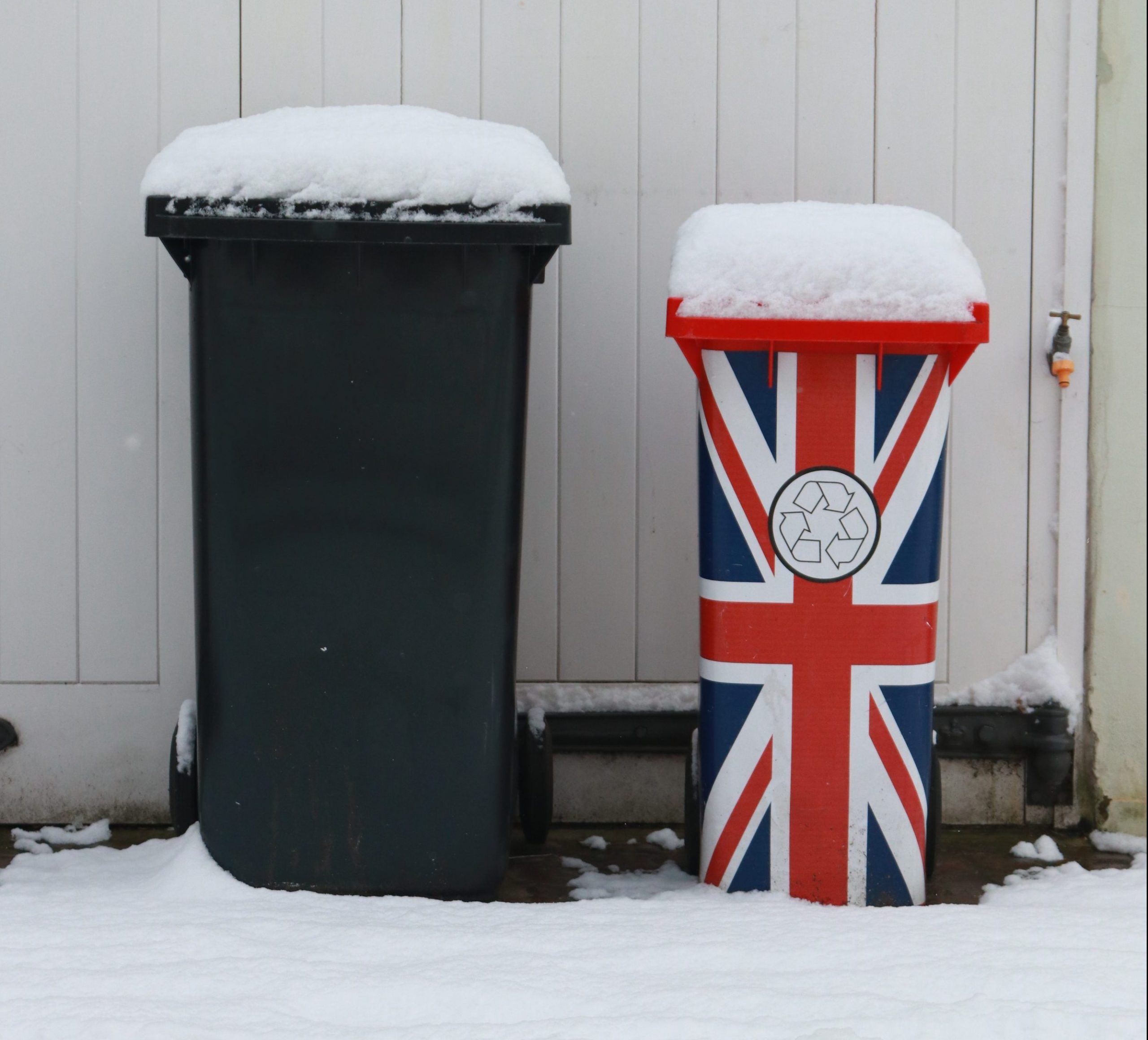 lixeiras com neve em cima, uma lixeira preta e a outra lixeira com a bandeira britanica