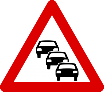 Placa de trânsito triangular com borda vermelha e três carros pretos alinhados, indicando “trânsito lento” ou possibilidade de congestionamento à frente.