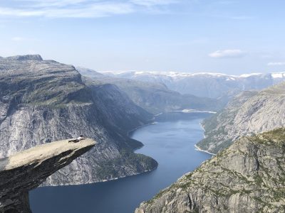 homem escalando, chegando deitado na ponta da pedra trolltunga muito alta com vista pro fiorde na noruega