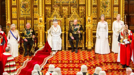 rainha elizabeth ii com coroa na cabeça e capa sentada no trono ao lado do principe philip e principe charles na camara dos lordes no parlamento britânico em londres