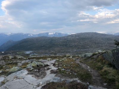campo aberto com pedras soltas e montanhas com neve ao fundo durante a trilha trolltunga no norte da noruega