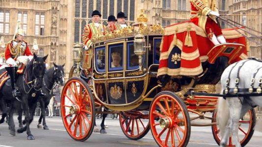 rainha elizabeth II andando em carruagem com cavalos guarda real escoltando ela em frente ao parlamento britanico em londres
