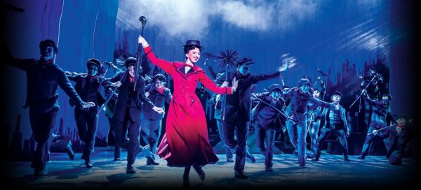 mary poppins de vestido mermelho, chapéu e guarda-chuva com atores dançando ao redor na peça de teatro mary poppins em londres