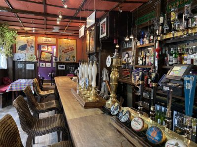balcão de pub em londres com opções de cerveja ale e lager, teto sem decoração, quadros na parede e toalha de mesa colorida