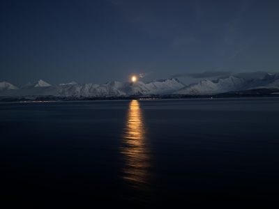 lua sob as montanhas com neve em frente ao mar do norte, no norte da noruega