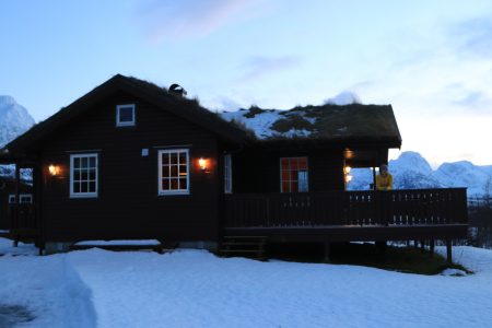 mulher na varanda de uma casa de madeira com neve no telhado e ao redor da casa no norte da noruega