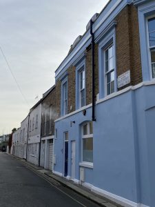 rua em notting hill com predio azul e de tijolos e placa escrito rua pottery lane, num passeio em notting hill