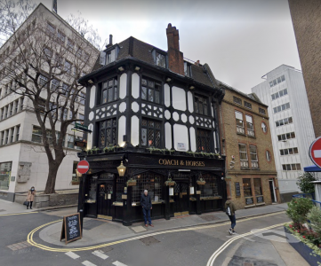 Pub tradicional inglês chamado Coach & Horses em esquina de rua urbana com fachada histórica em preto e branco.