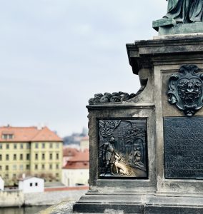 Relevo em bronze de um cão na base da estátua de São João Nepomuceno na Ponte Carlos, Praga, desgastado e brilhante por turistas que acariciam em busca de sorte.