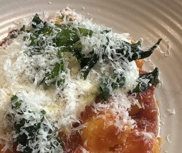 Nhoque com molho de tomate e queijo parmesão por cima em prato com fundo branco