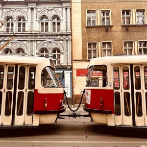 Tram vermelho de transporte público passando por rua de paralelepípedos com arquitetura histórica em Praga